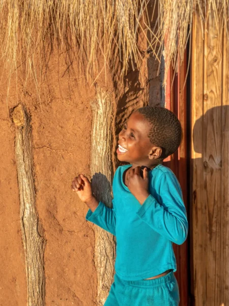 Glad dreng ved hytte i landsby i Botswana, Afrika